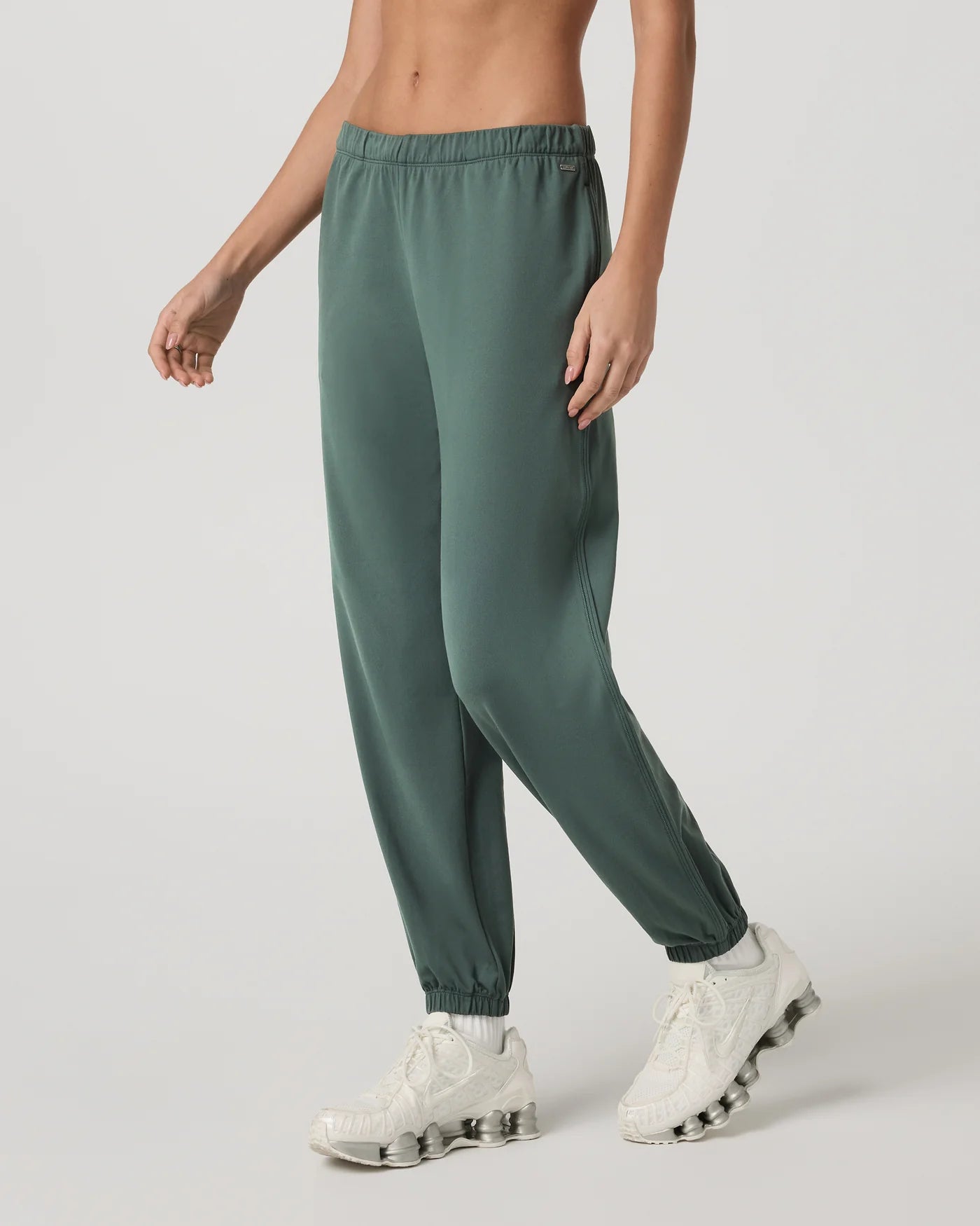 Person wearing green jogger pants and white sneakers on a light gray background