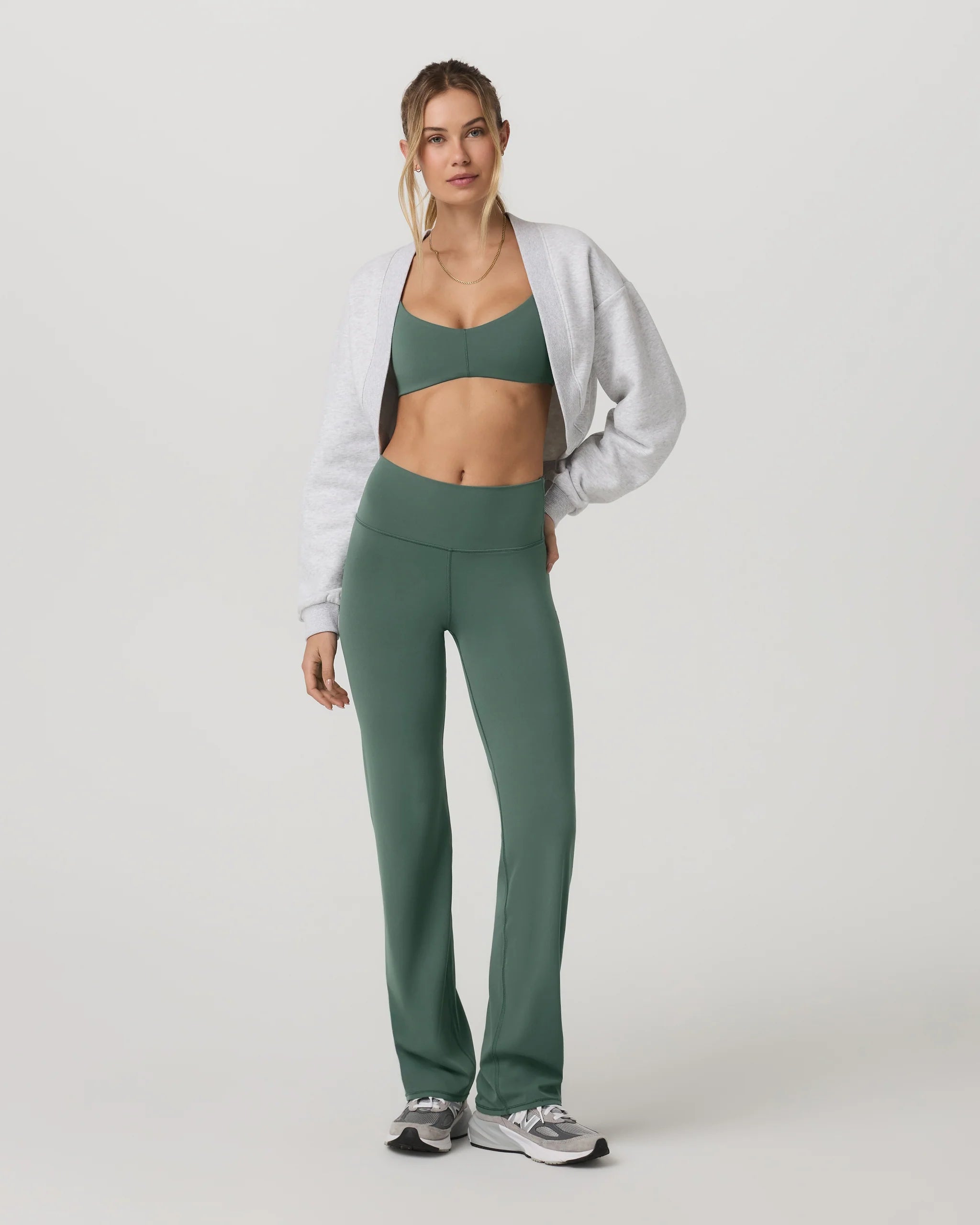 Woman wearing a green athletic outfit with a white jacket on a white background