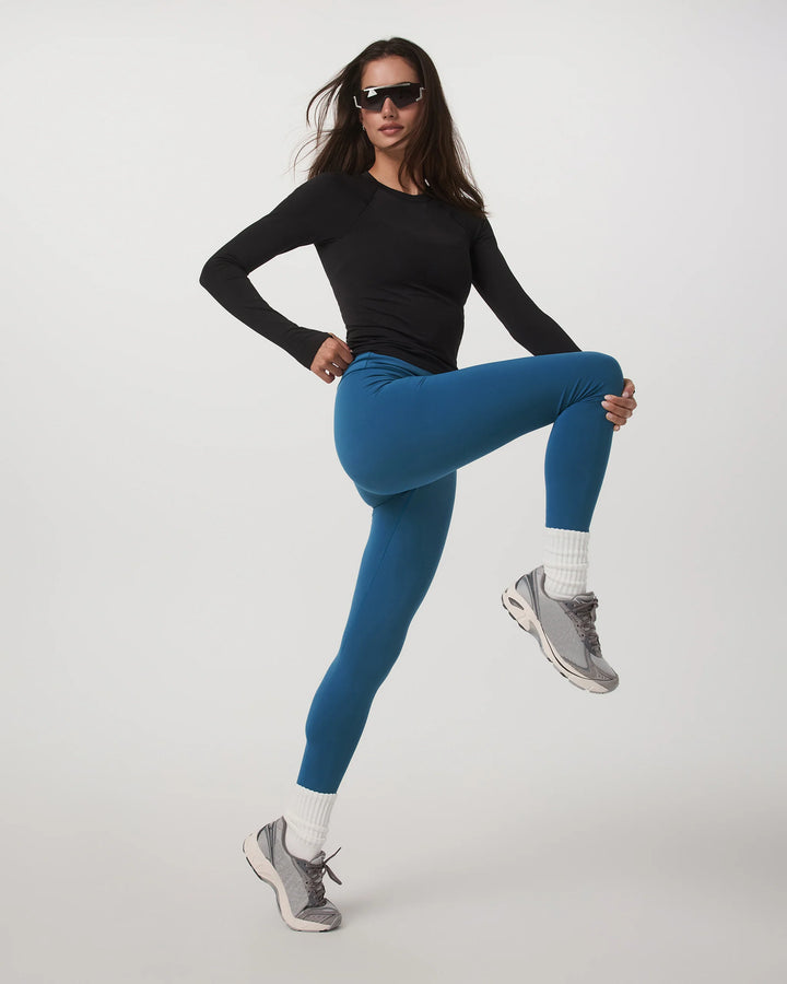 Woman in black long-sleeve top and blue leggings posing on a white background