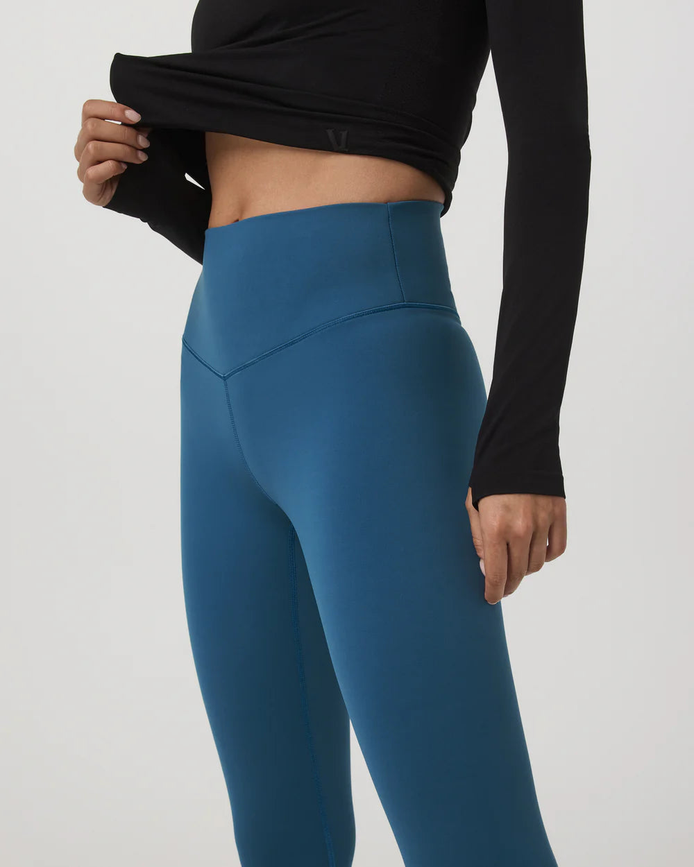 Person wearing blue leggings and black long-sleeve top on a white background