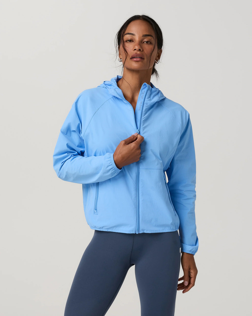 Woman wearing a light blue jacket and dark blue leggings on a gray background