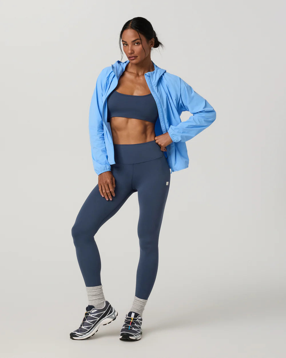 Woman wearing a blue athletic jacket and leggings on a light gray background