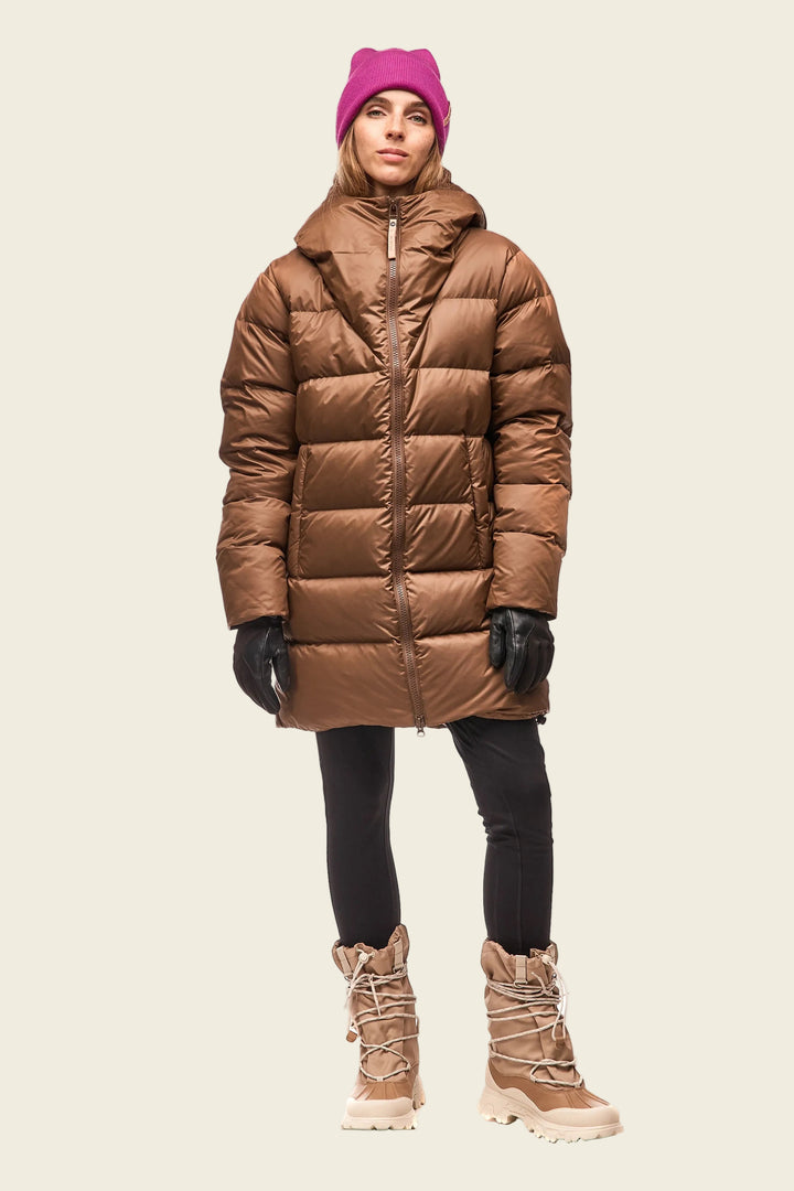 Person wearing a brown puffer coat, pink beanie, black gloves, and beige boots on a white background