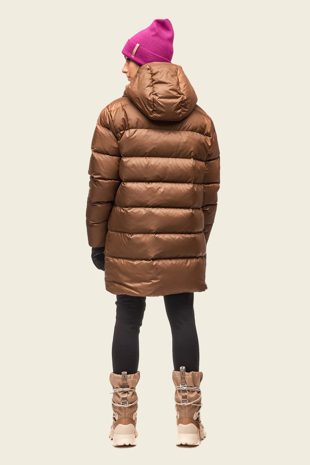 Person wearing a brown puffer coat, black leggings, and pink beanie on a white background