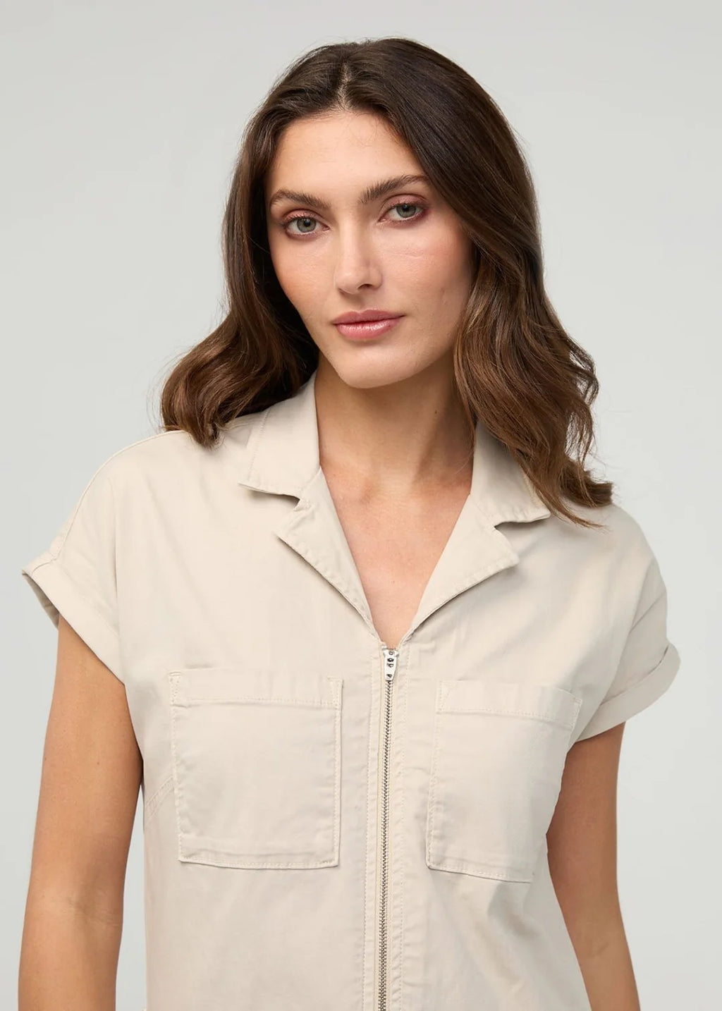 Woman wearing a beige sleeveless jacket with a zipper on a plain background