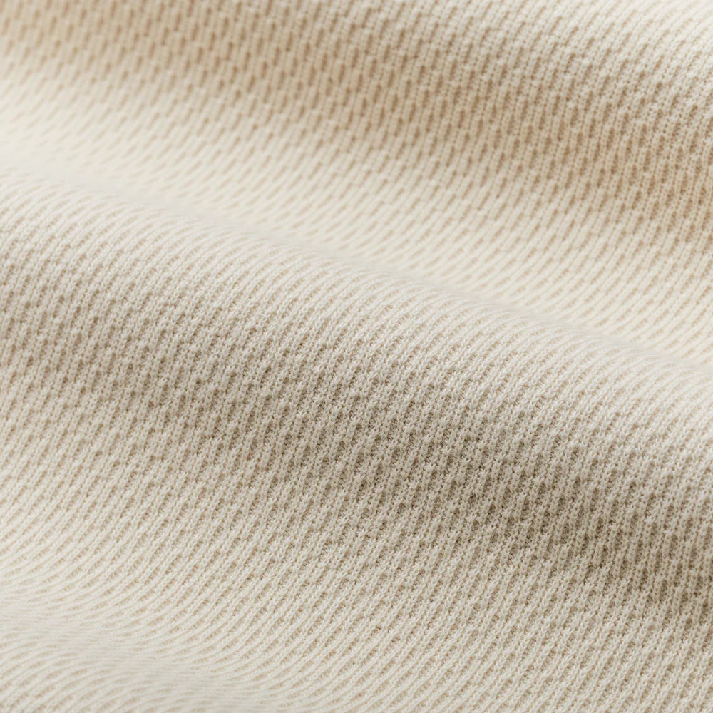 Close-up of a ribbed knit fabric in a warm cream or off-white color, showing the detailed texture and folds.