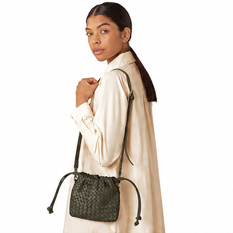 A model wearing a cream-colored long-sleeve shirt and a dark olive green woven bucket bag with a drawstring strap, photographed against a solid white background.