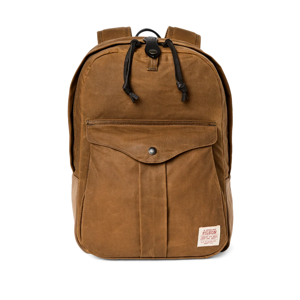 A brown waxed canvas backpack with a front flap pocket, black drawstrings, and a small white Filson brand patch on the bottom right, shown against a plain white background.