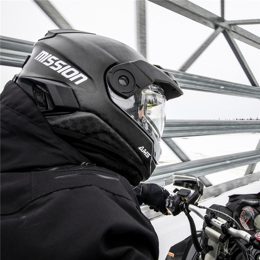 Person wearing a black 'Mission' helmet on a Snowmobile outdoors.