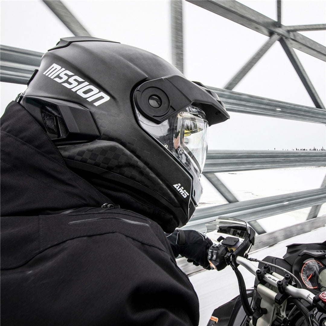Person wearing a black 'Mission' helmet on a Snowmobile outdoors.