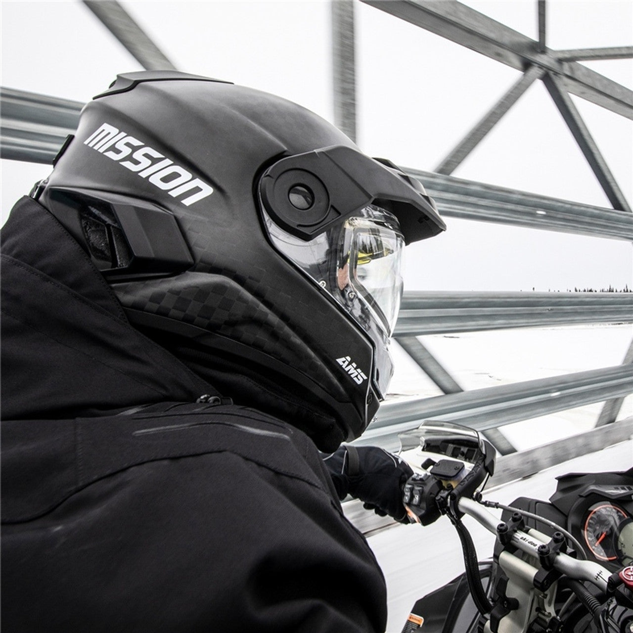 Person wearing a black 'Mission' helmet on a Snowmobile outdoors.