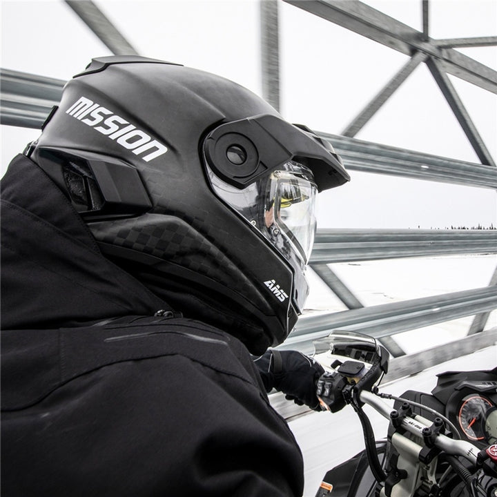 Person wearing a black 'Mission' helmet on a Snowmobile outdoors.