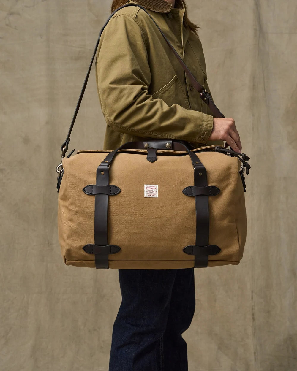 Person holding a brown leather-bound bag against a beige background