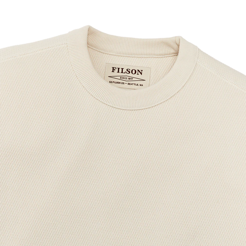 Close-up of a cream-colored crewneck sweatshirt by Filson, showing the ribbed collar and the brand label inside.