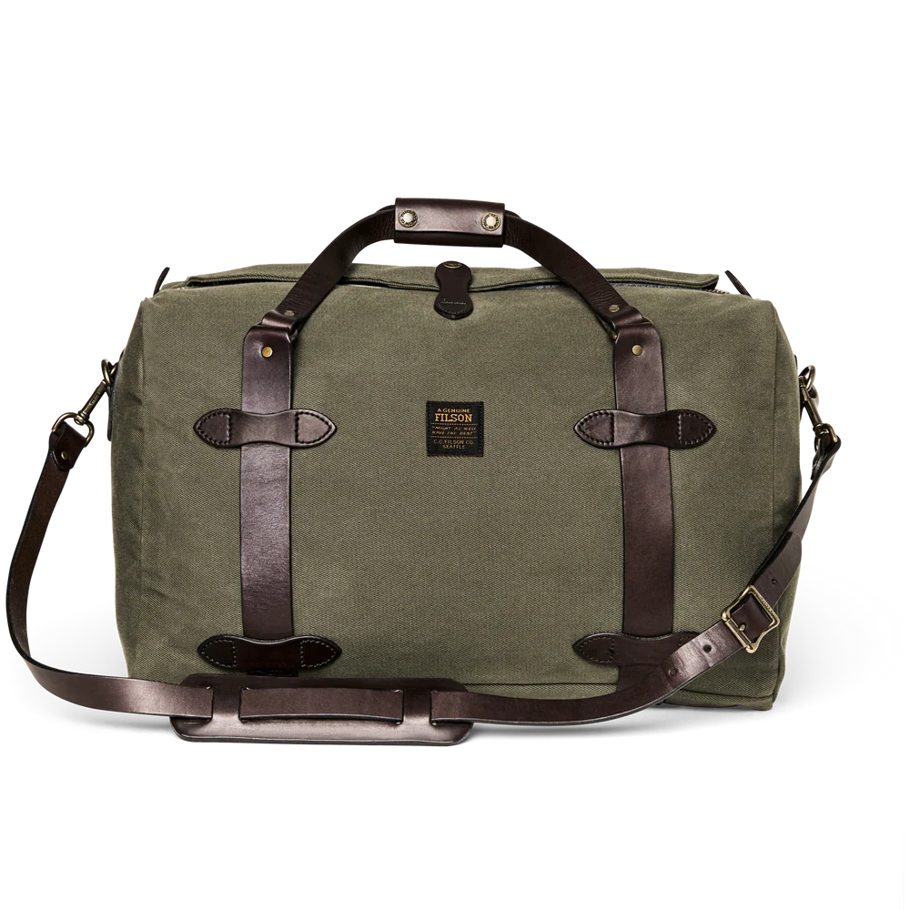 An olive green canvas duffel bag with dark brown leather straps and handles, featuring a small Filson brand patch on the front, set against a plain white background.