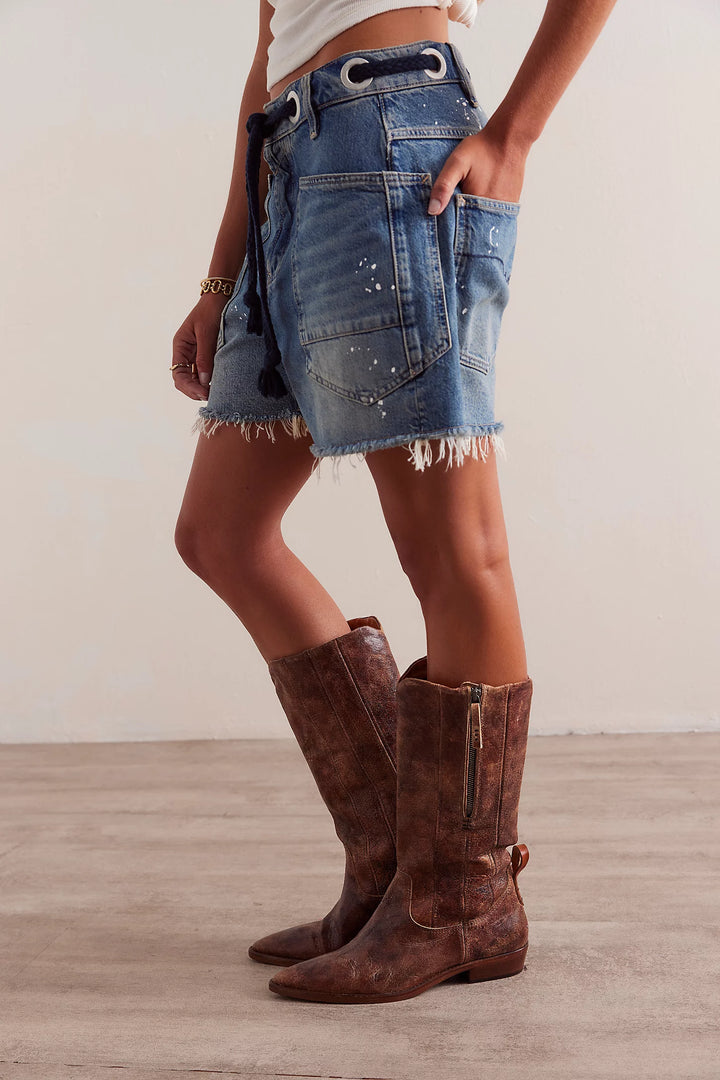 Person wearing a denim skirt and brown knee-high boots on a plain background