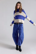 Woman wearing a blue and white striped sweater with blue jeans on a plain background