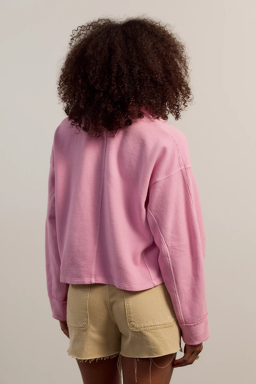 Person wearing a pink sweater and beige shorts from behind on a plain background