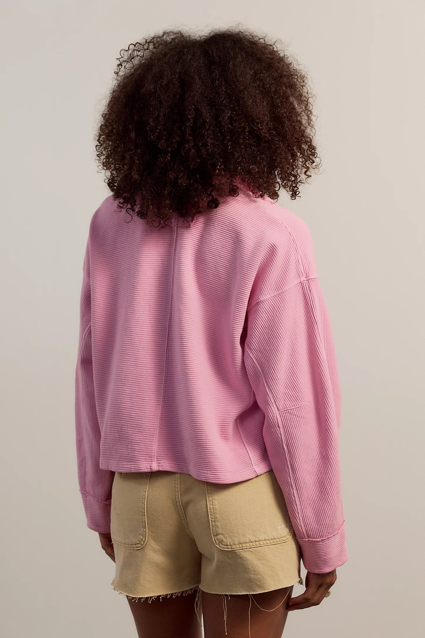 Person wearing a pink sweater and beige shorts from behind on a plain background