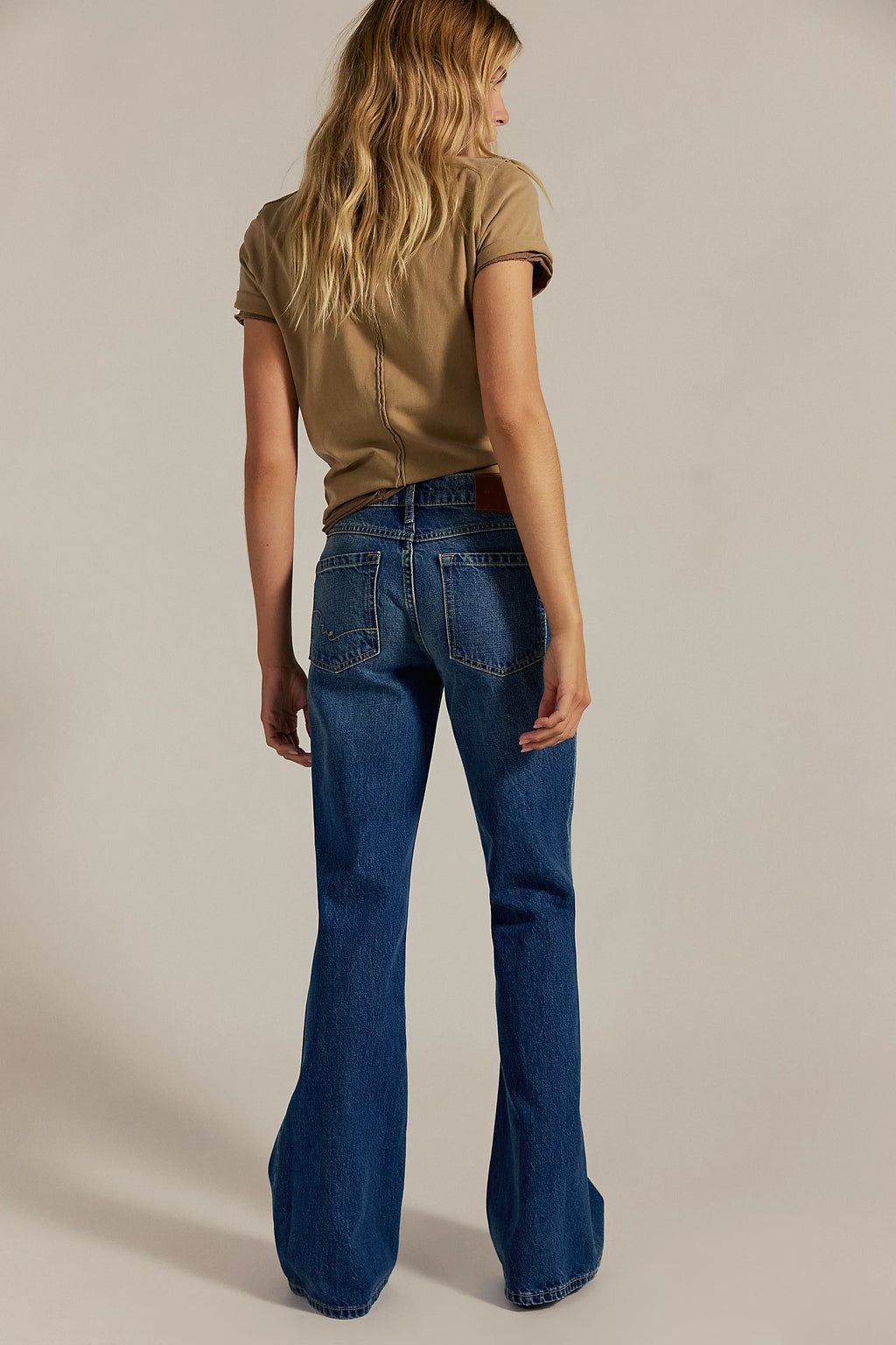 Person wearing a brown top and blue flared jeans on a beige background