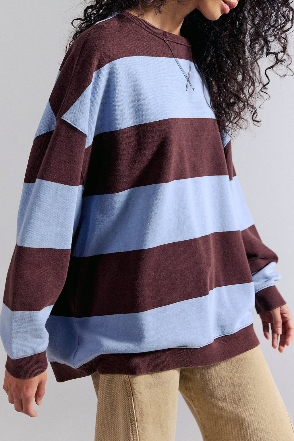 Person wearing a striped sweater with brown and light blue horizontal stripes on a plain background