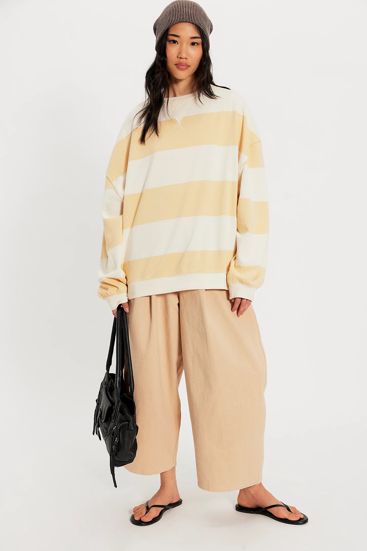 Person wearing a yellow and white striped sweater with beige pants on a white background
