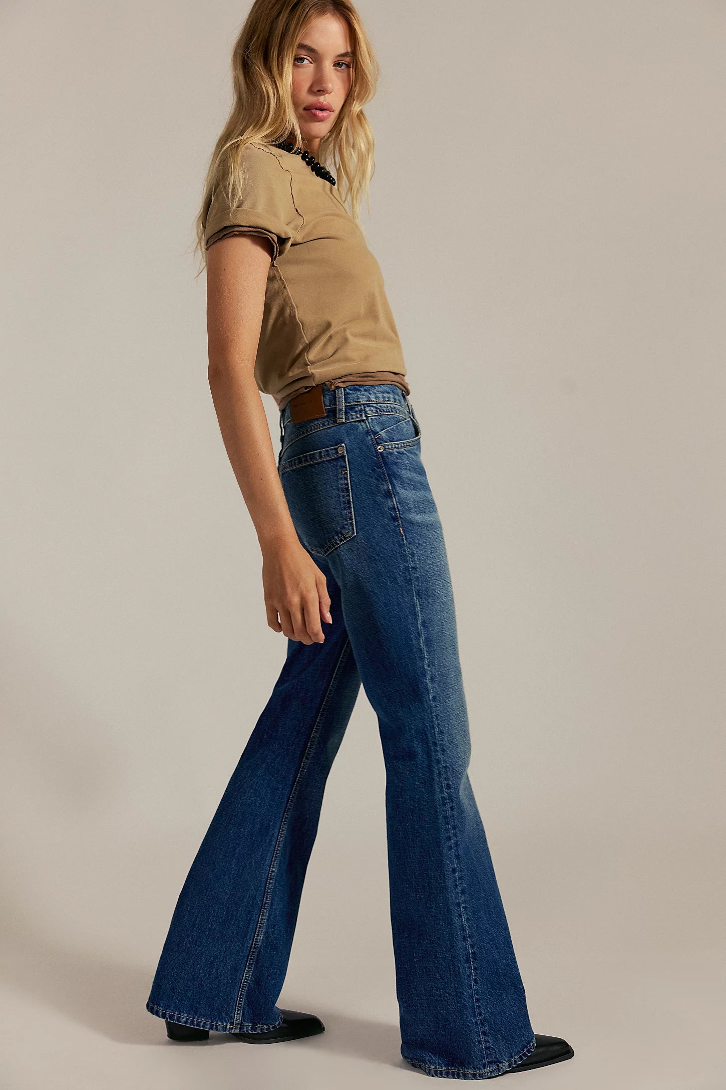 Woman wearing a beige top and blue flared jeans on a plain background