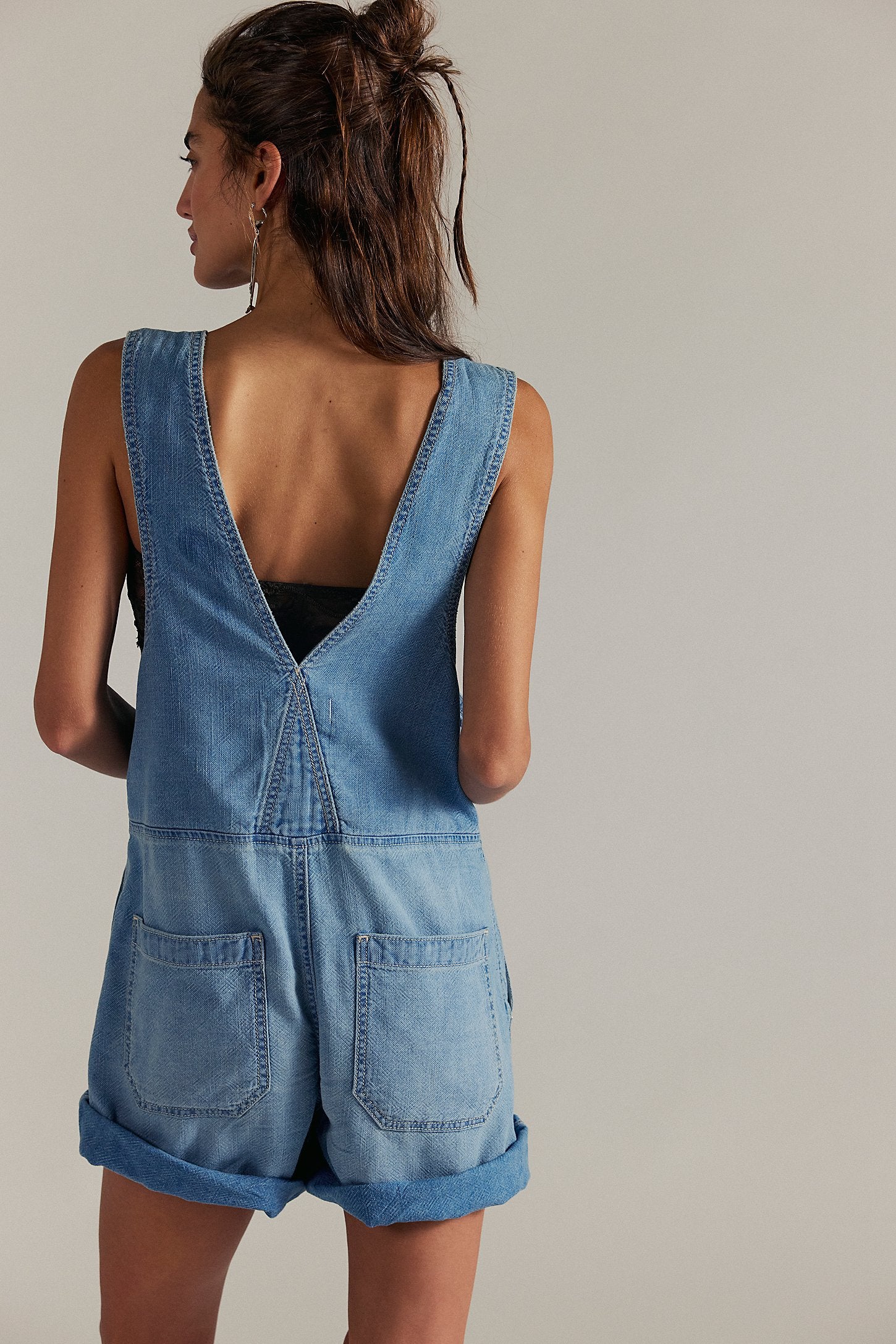 Woman wearing a blue denim romper against a neutral background