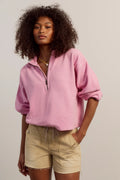 Woman wearing a pink sweater and beige shorts against a plain background