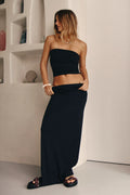 Woman wearing a black strapless top and long black skirt against a neutral background