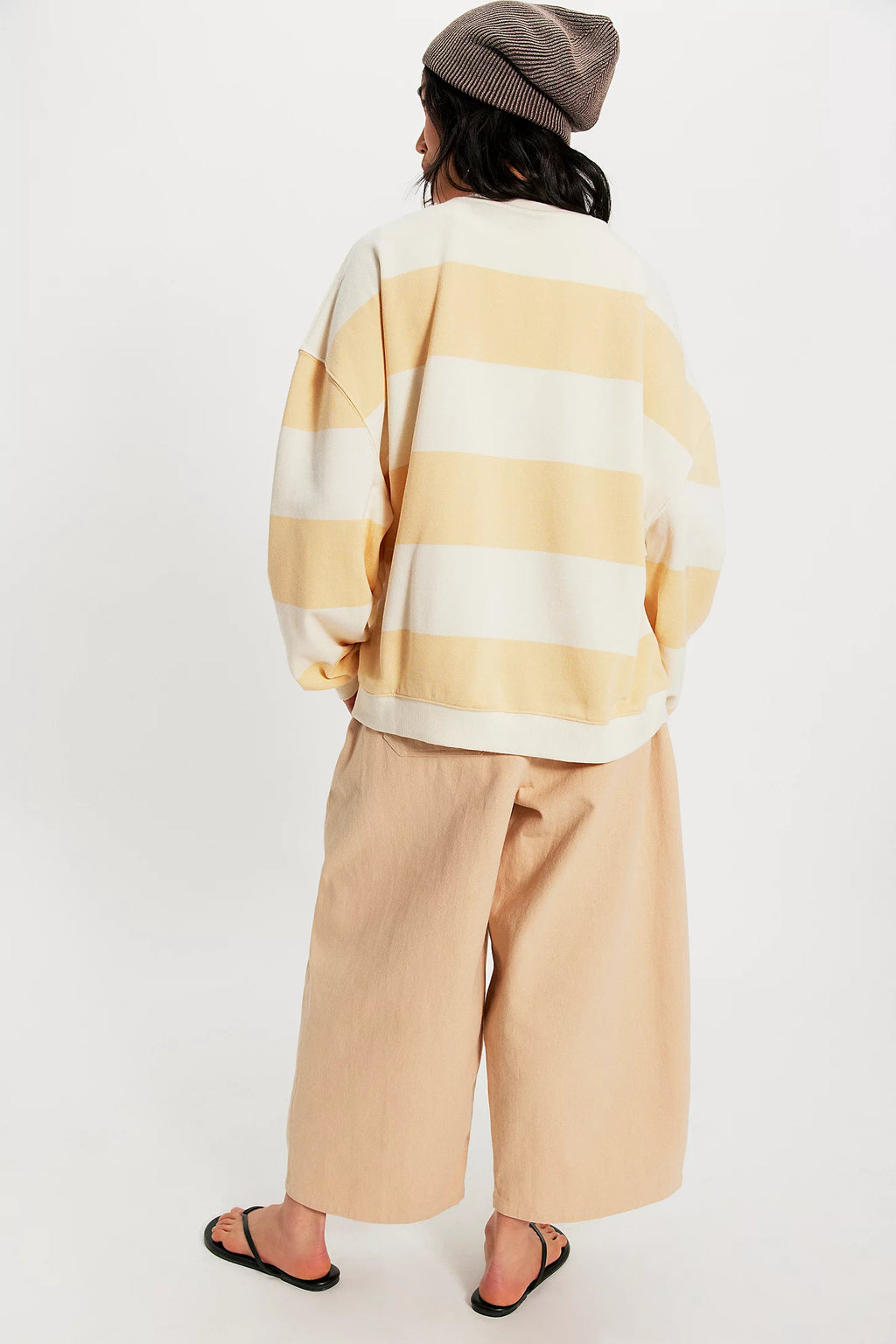 Person wearing a yellow and white striped sweater and beige pants on a white background