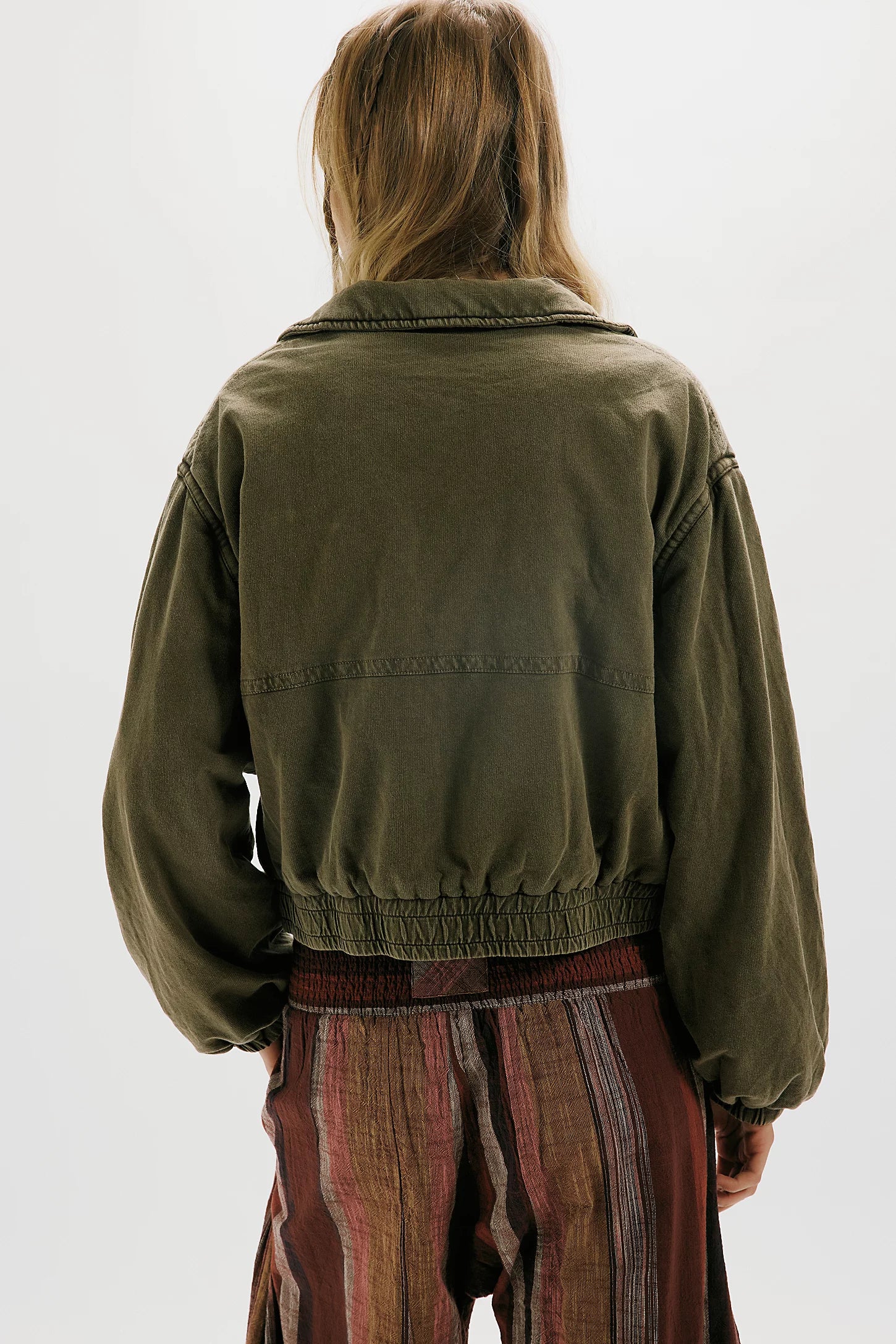 Person wearing a green jacket and striped pants on a white background