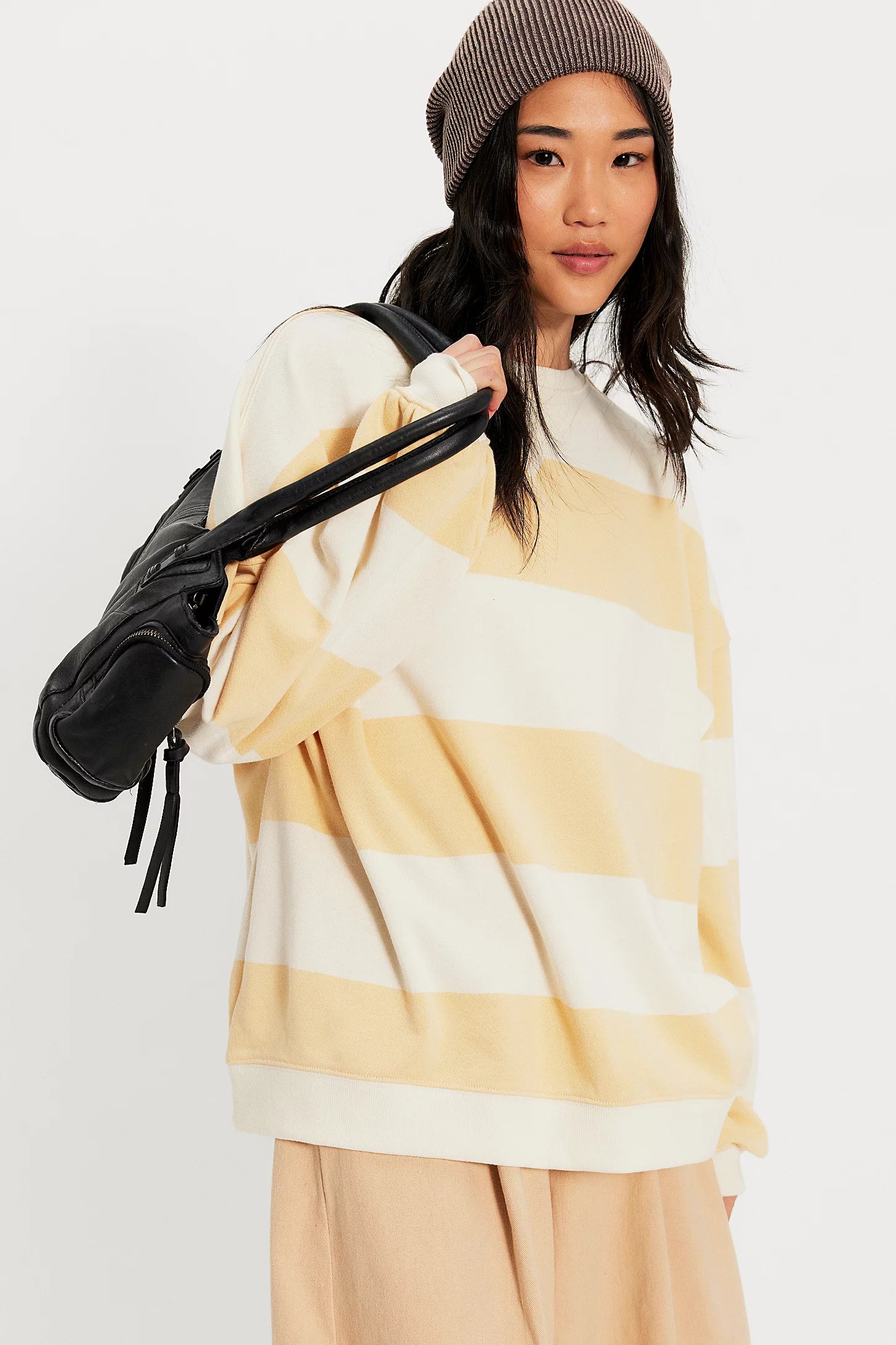 Woman wearing a yellow and white striped sweater with a black backpack on a white background