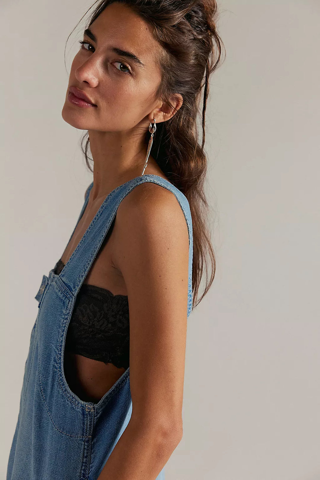 Woman wearing a denim overalls and black top against a plain background