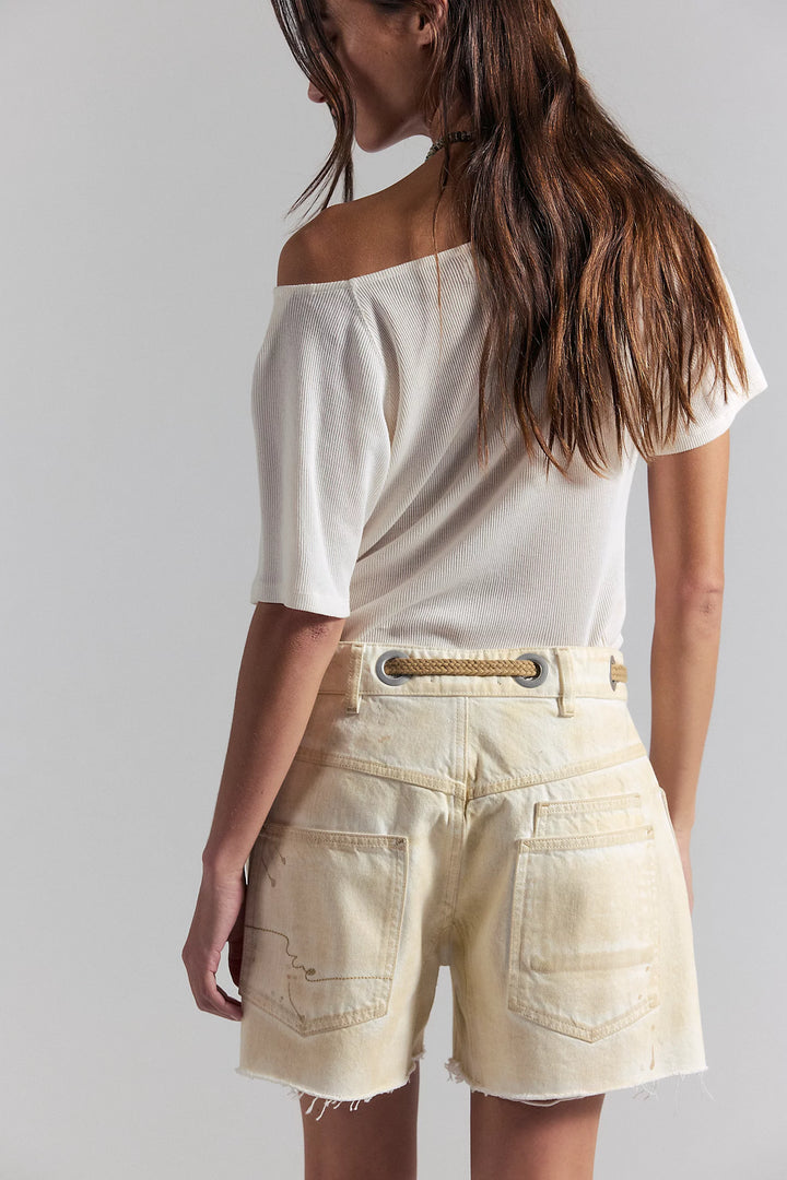 Woman wearing a white off-shoulder top and beige shorts against a plain background