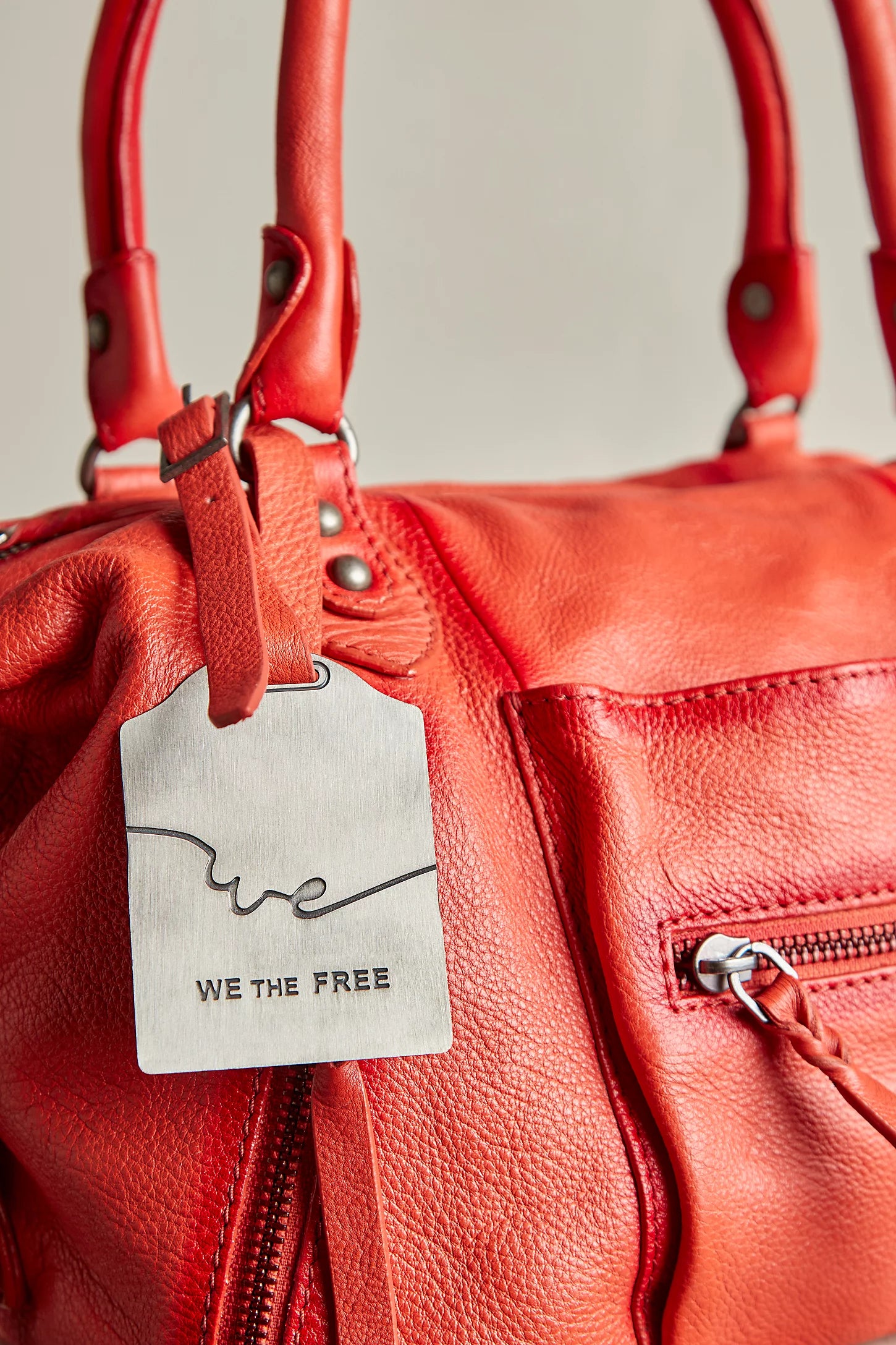 Red leather handbag with a 'WE THE FREE' tag on a neutral background