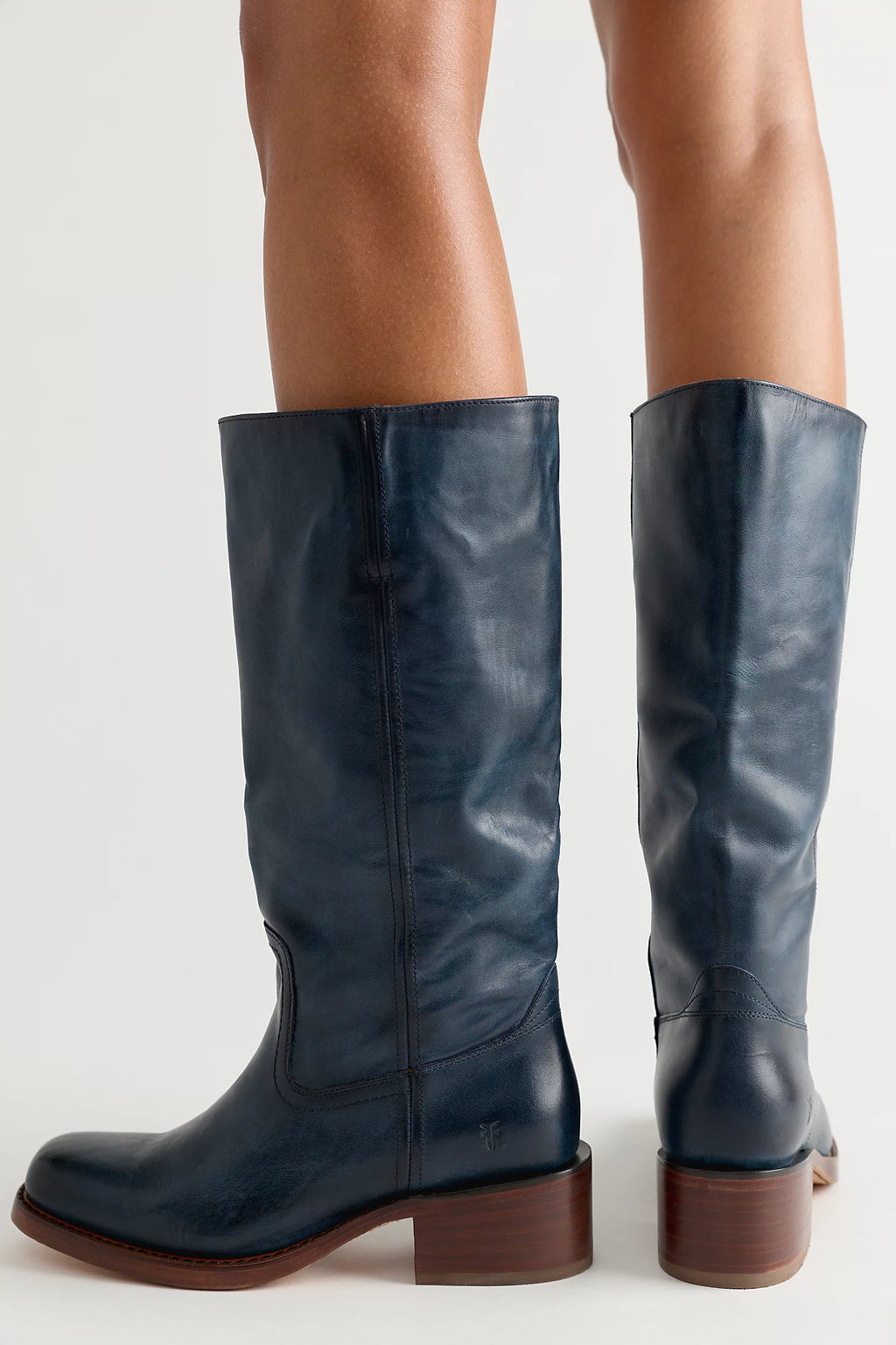 A pair of dark navy blue leather knee-high boots with brown stacked block heels, shown on a model's legs against a light gray studio background.