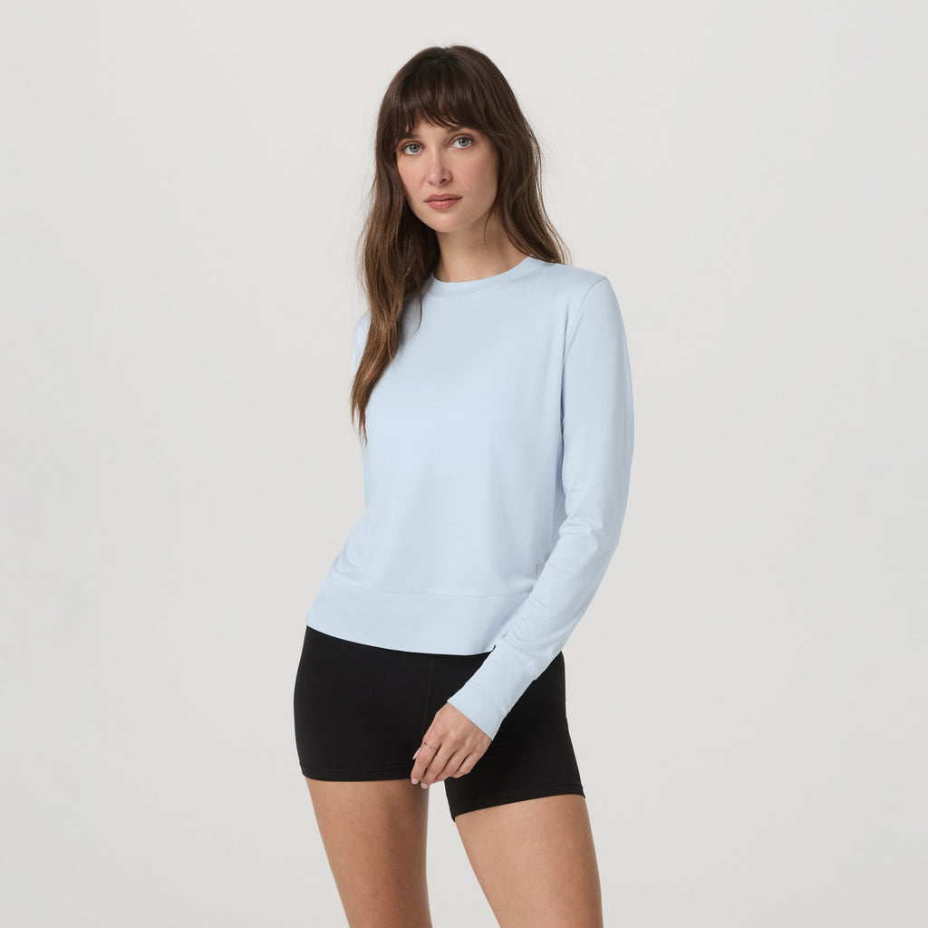 Woman wearing a light blue long-sleeve top and black shorts on a white background