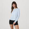 Woman wearing a light blue long-sleeve top and black shorts on a white background