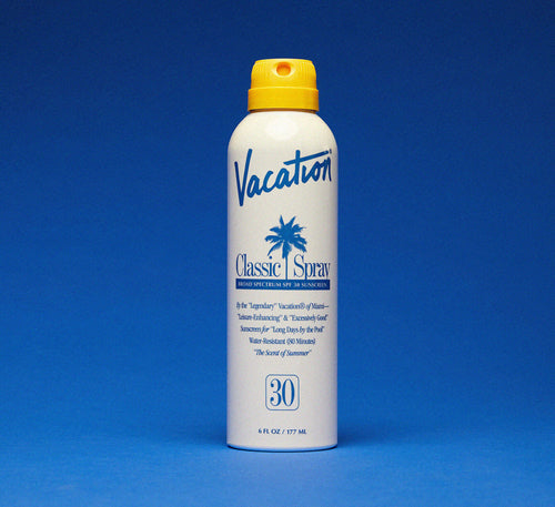 Vacation Classic Spray sunscreen bottle with yellow cap on a blue background