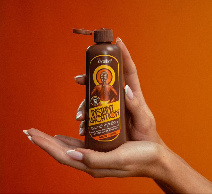 Hand holding a bottle of 'Instant Vacation' bronzing lotion against an orange background