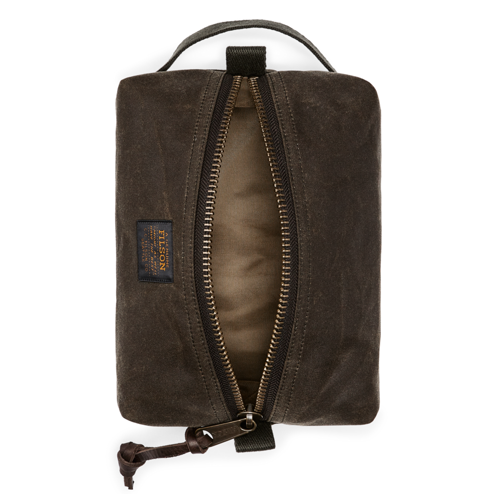A dark brown waxed canvas zippered pouch with an open zipper showing a tan interior, featuring a top handle and a small brand patch on the side.