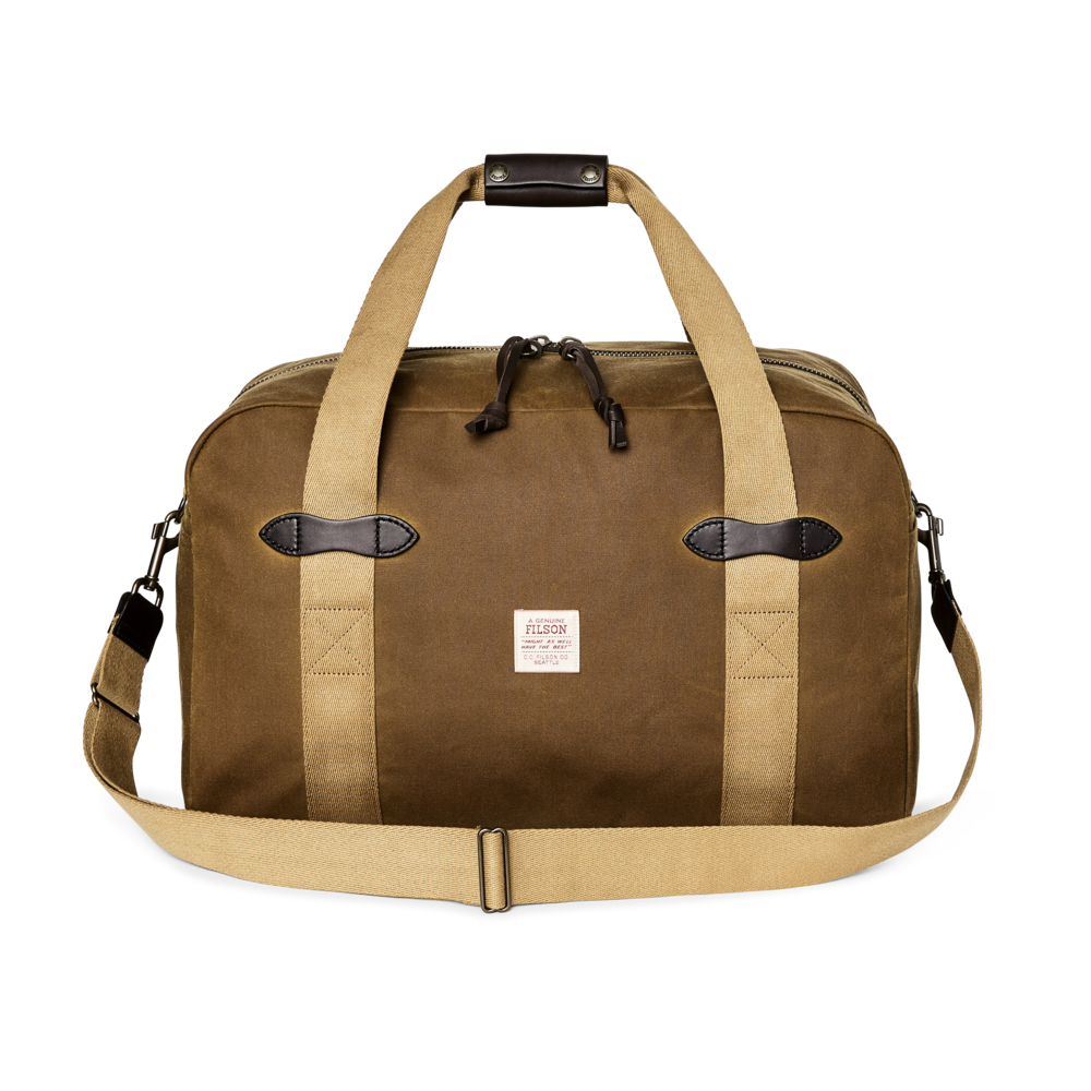 A brown waxed canvas duffel bag with tan webbing handles and a matching adjustable shoulder strap, featuring dark brown leather accents and a small white brand label on the front.