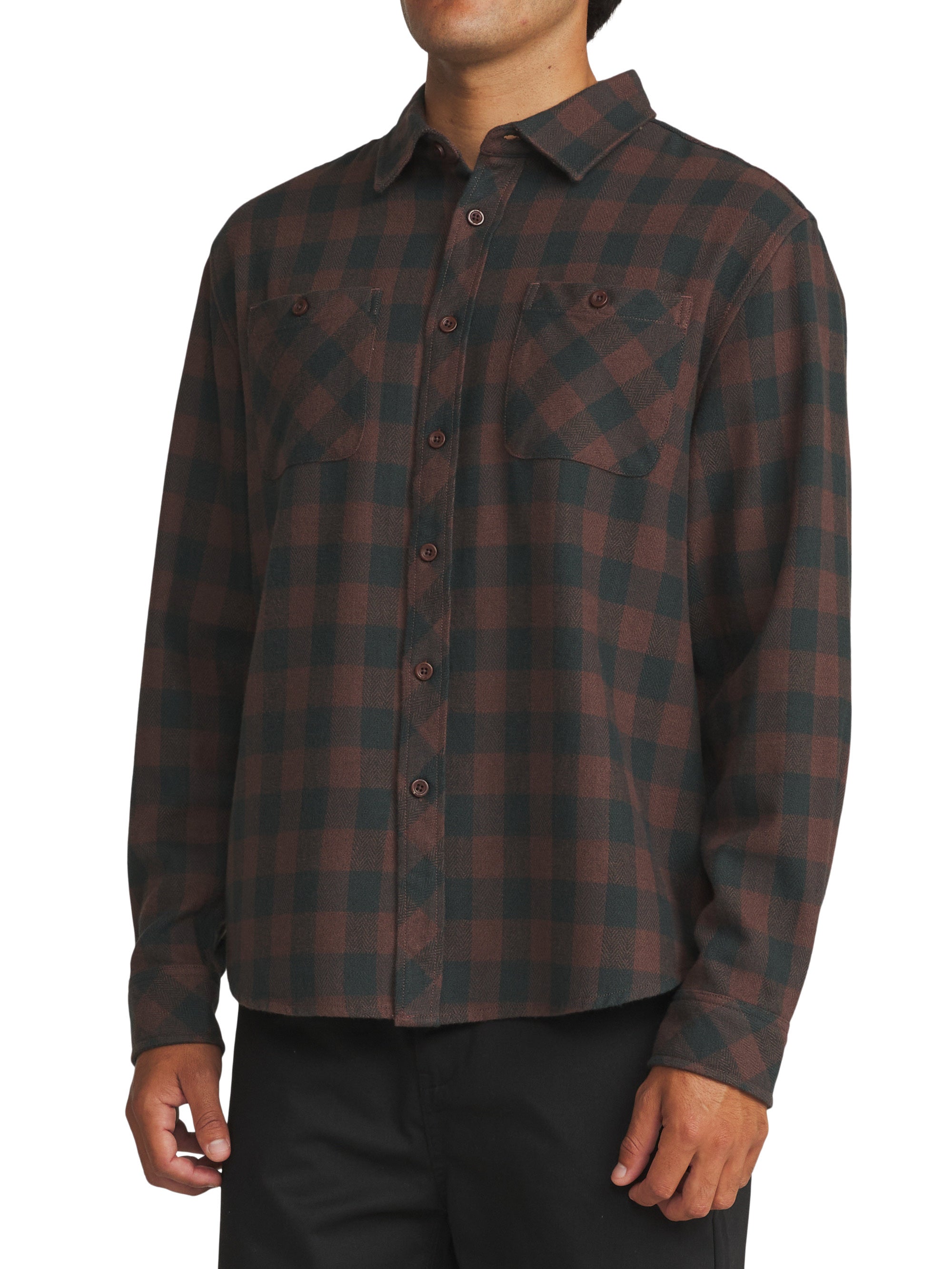 A man wearing a long-sleeve button-up flannel shirt with a dark brown and black buffalo plaid pattern, paired with black pants, against a plain white background.