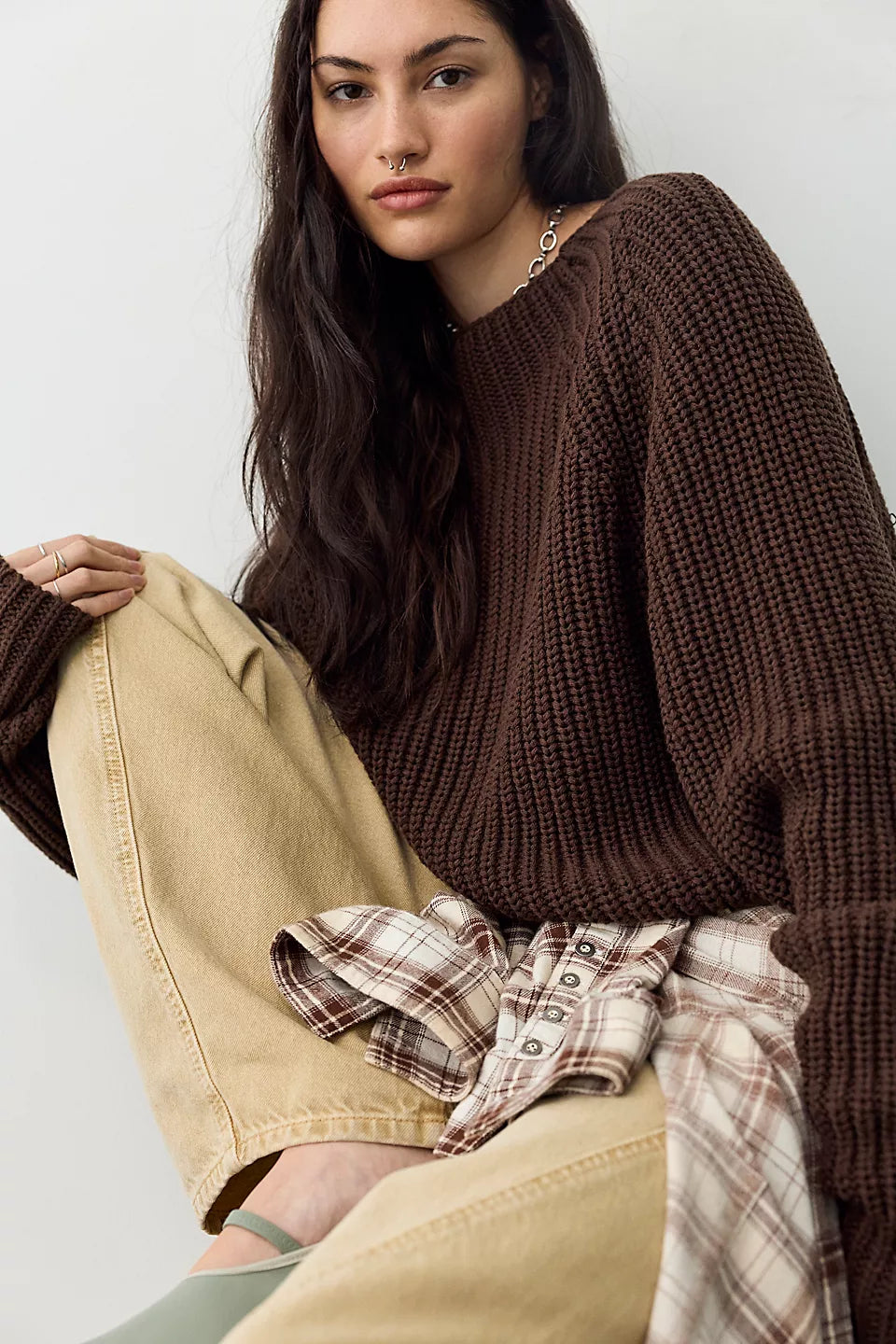woman modeling dark brown sweater paired with cream colored pants and brown and cream plaid shirt tied around her waist.