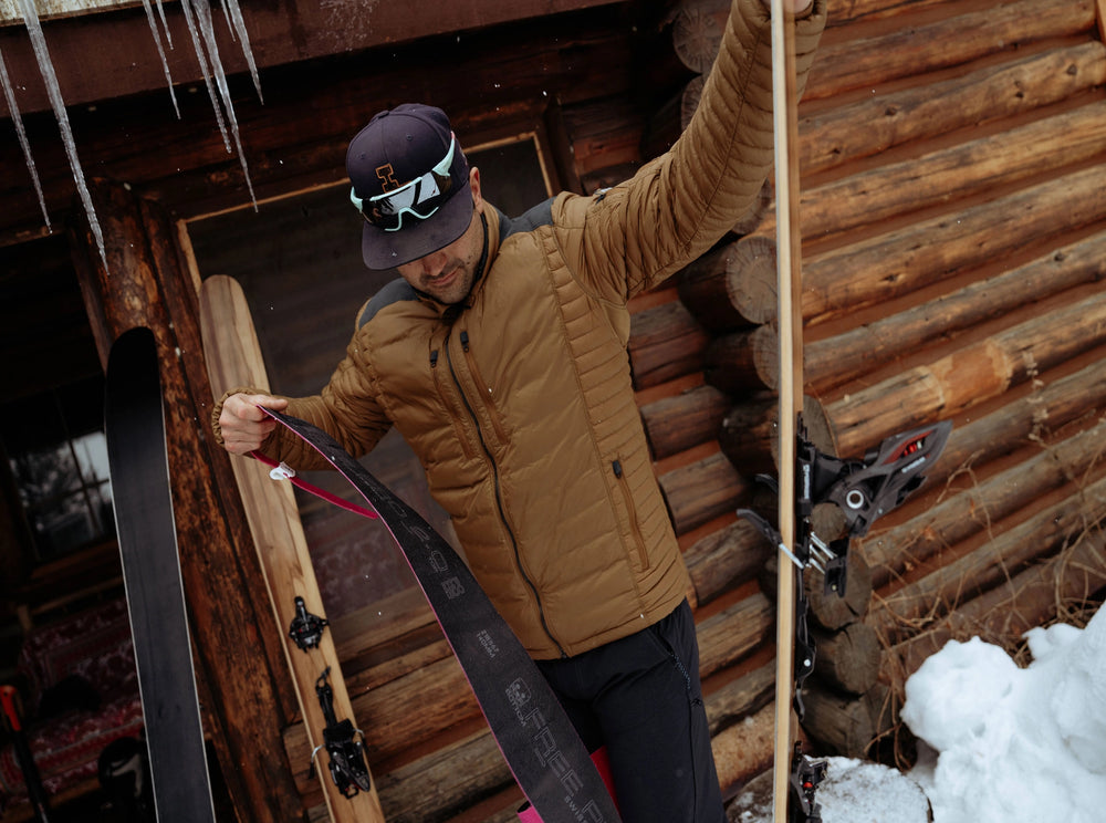 Man with skis standing in front of a wooden cabin with snow on the ground