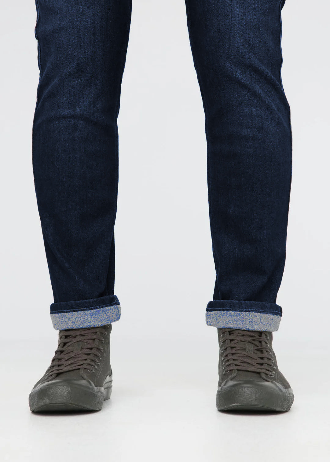 Dark blue jeans with rolled-up cuffs and gray sneakers on a white background