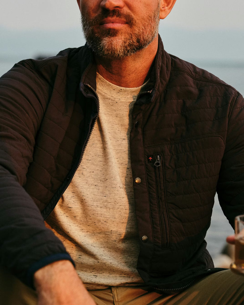 Man wearing a dark quilted jacket by the water
