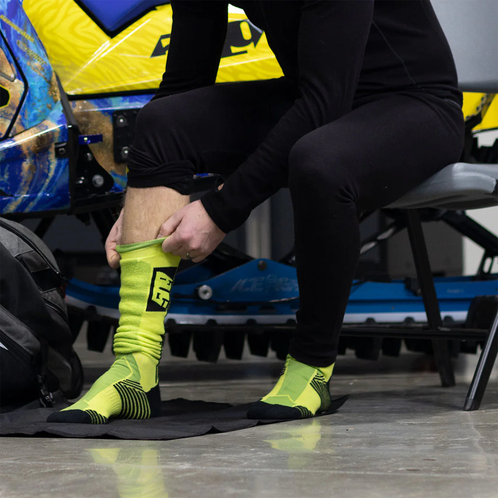 Person wearing bright green socks with black accents, sitting on a chair with a motorcycle in the background.