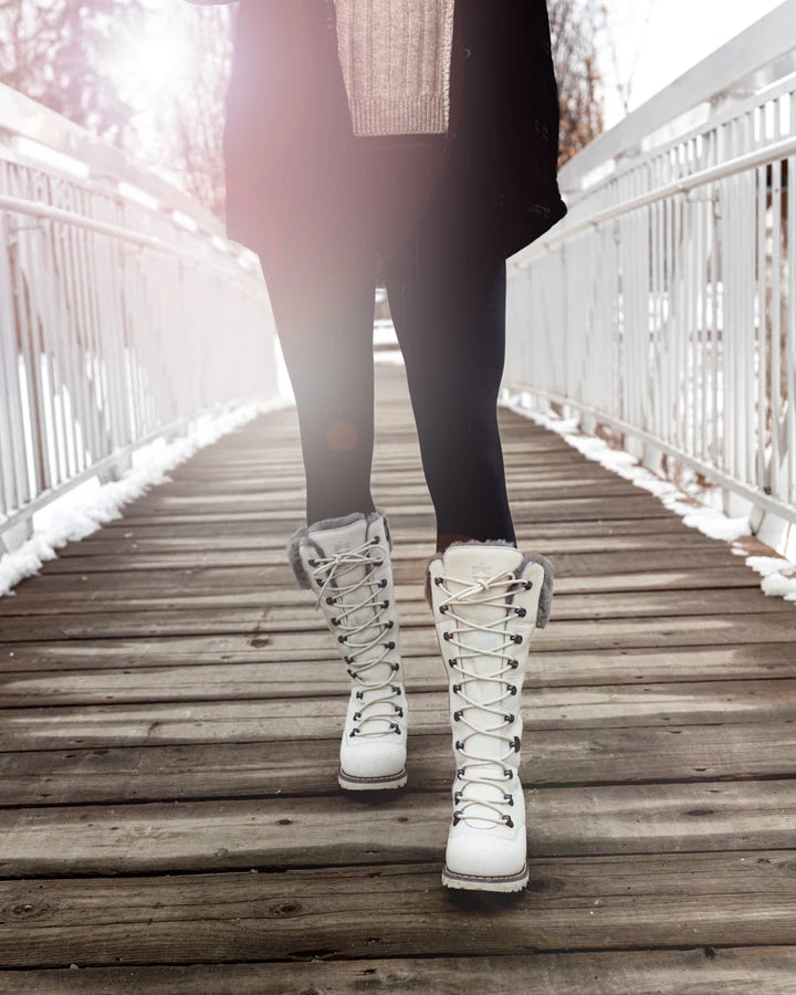 Person wearing white winter boots on a wooden bridge with snow-covered ground.